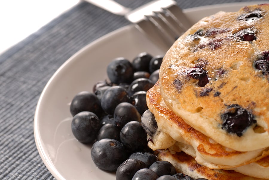 A plate of pancakes with fresh blueberries and syrup